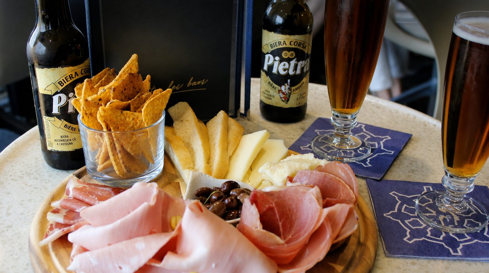 Un tavolo servito secondo lo standard: «Carte des bars», tagliere, bevande sui sottobicchieri con il logo Corsica Ferries.